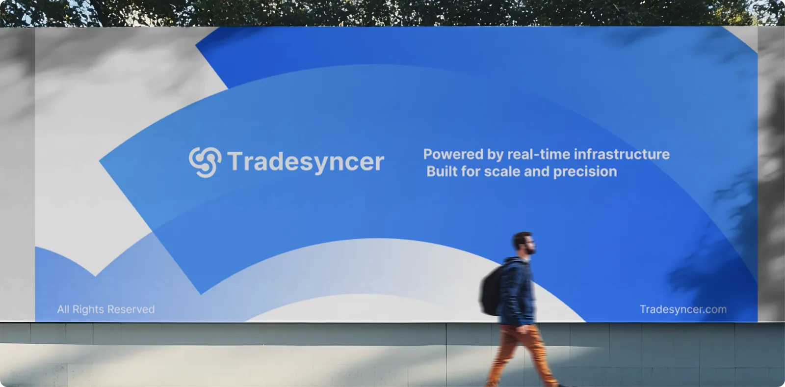 Tradesyncer billboard on a street wall: the logo in white on large blue arcs with the line “Powered by real-time infrastructure. Built for scale and precision.” A man with a backpack walks past